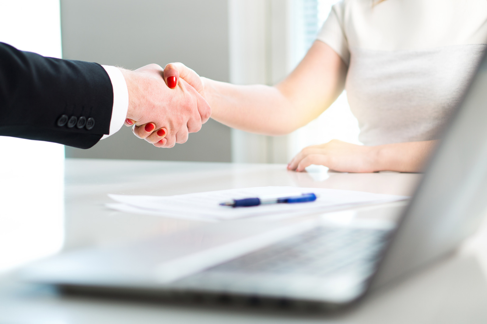Business man and woman shaking hands after successful job interview or meeting. Young applicant making contract of employment. Employer hiring new employee. Handshake in office.